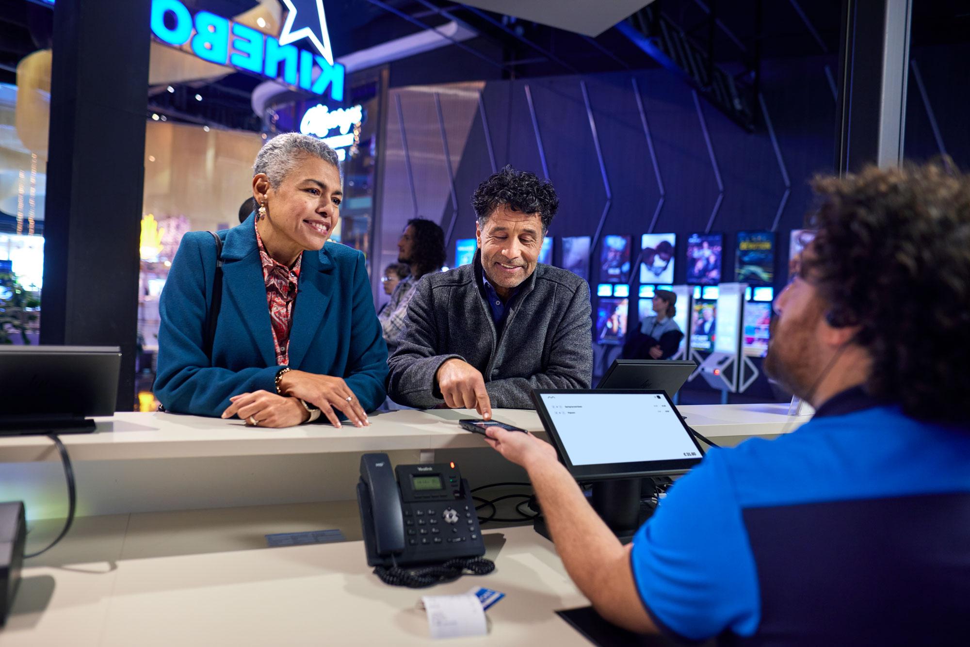 Visitantes del cine pagando boletos y confirmando puntos de fidelidad en el terminal S1E de Adyen.