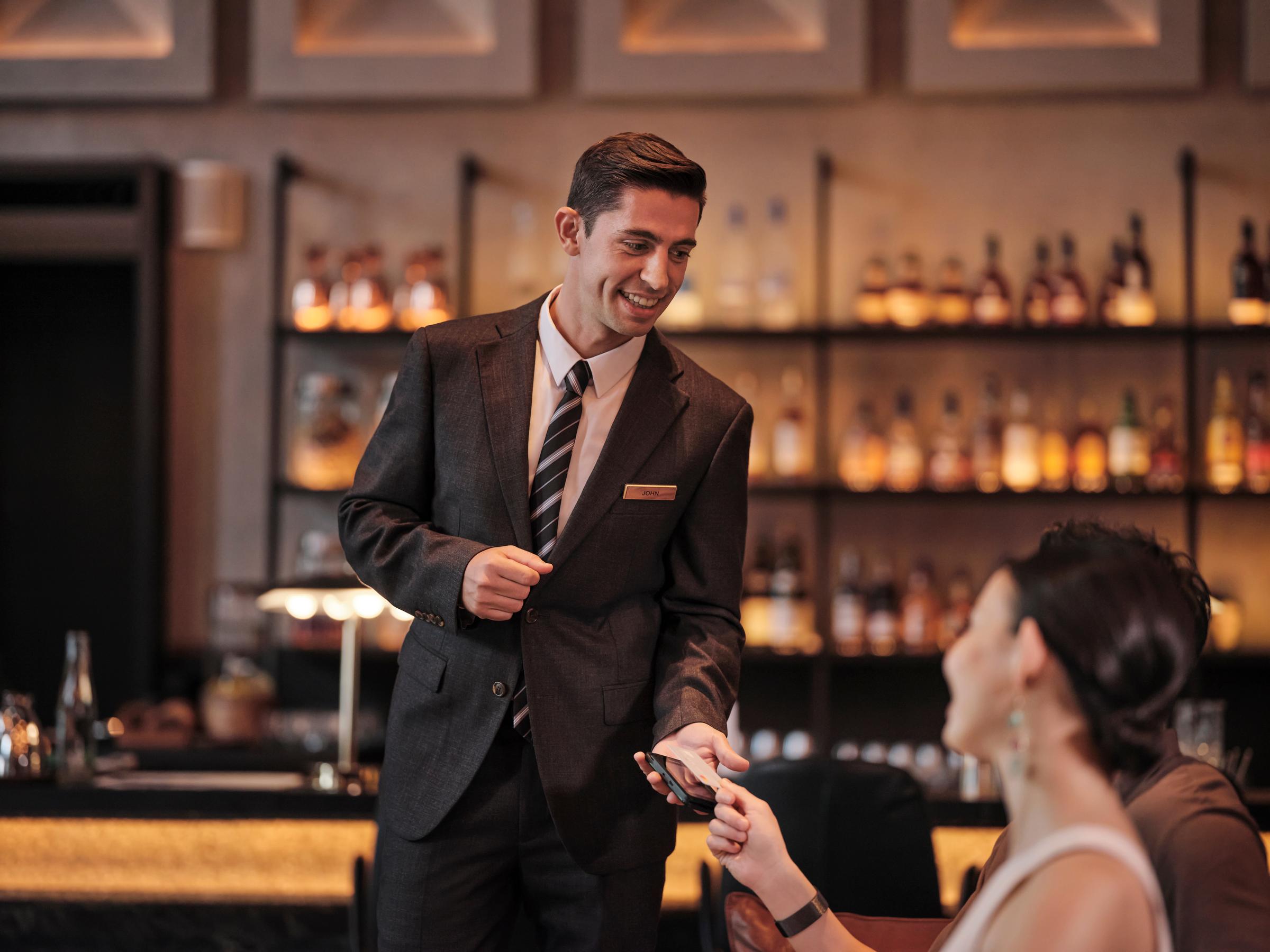 A  woman in a hotel bar paying for their drinks by tapping a card on Adyen's terminal.