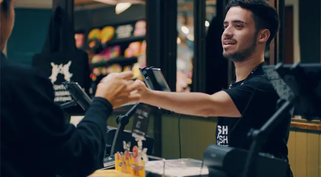 Smiling cashier handing over a portable card payment device to a customer.