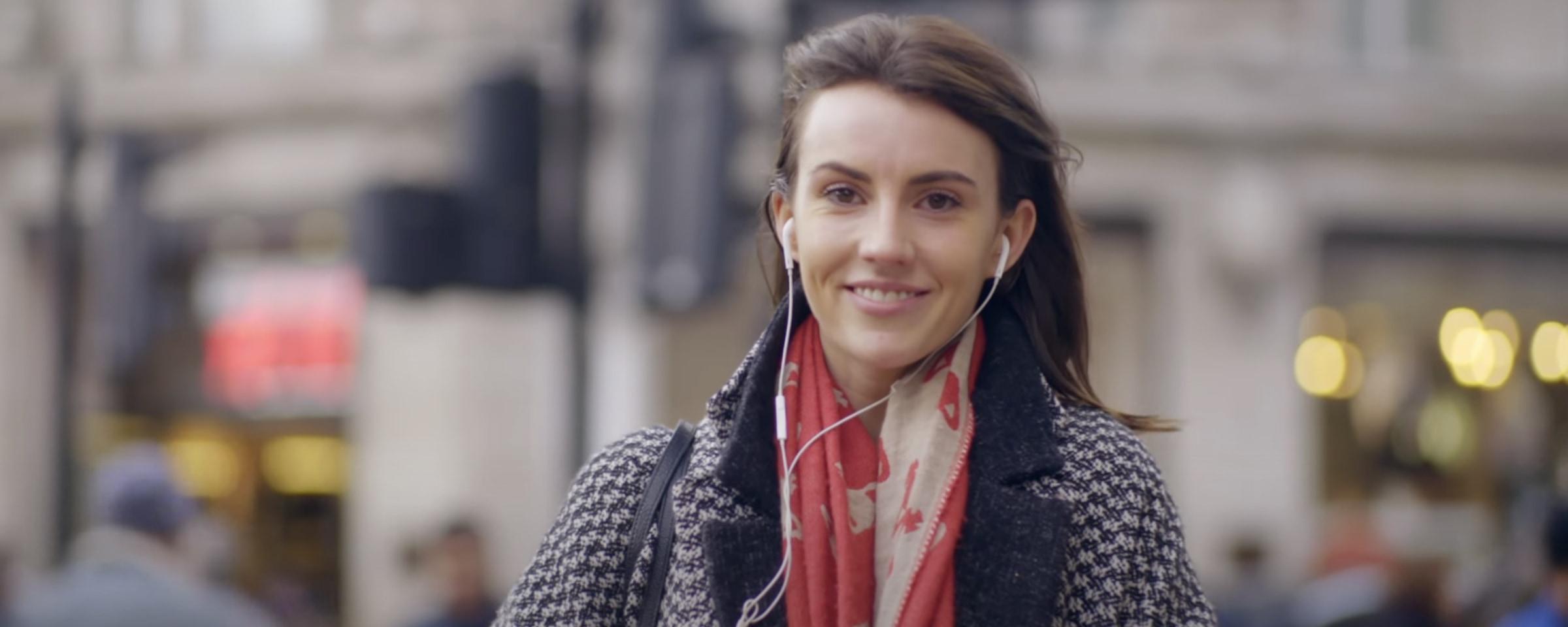 Smiling woman with earphones walking on a city street.