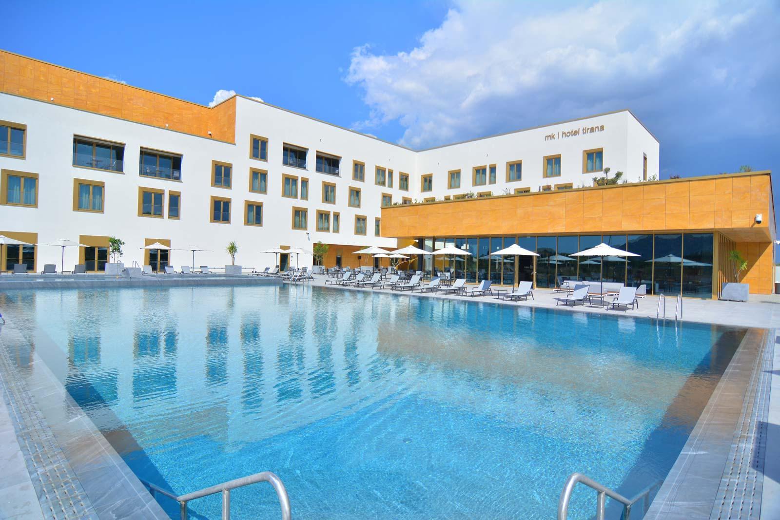 MK Hotel building exterior with large swimming pool and loungers under a blue sky.