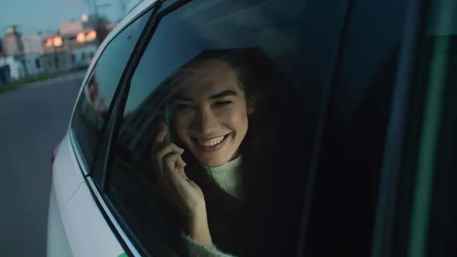Mulher sorridente a falar ao telefone dentro de um carro durante a noite.