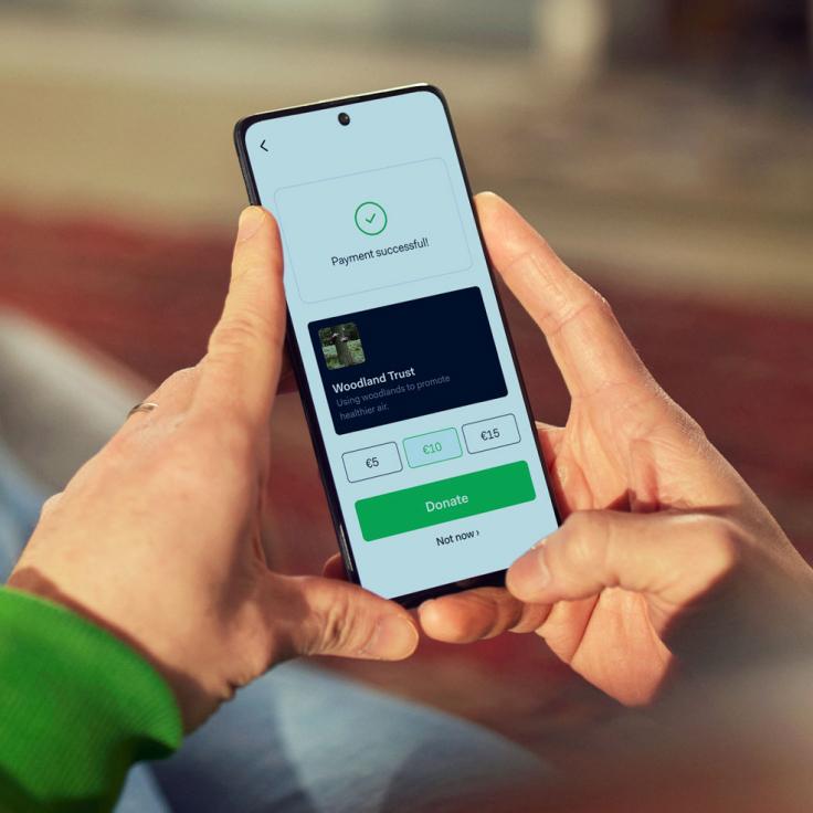 Person holding a smartphone displaying a successful payment notification for a donation to Woodland Trust.