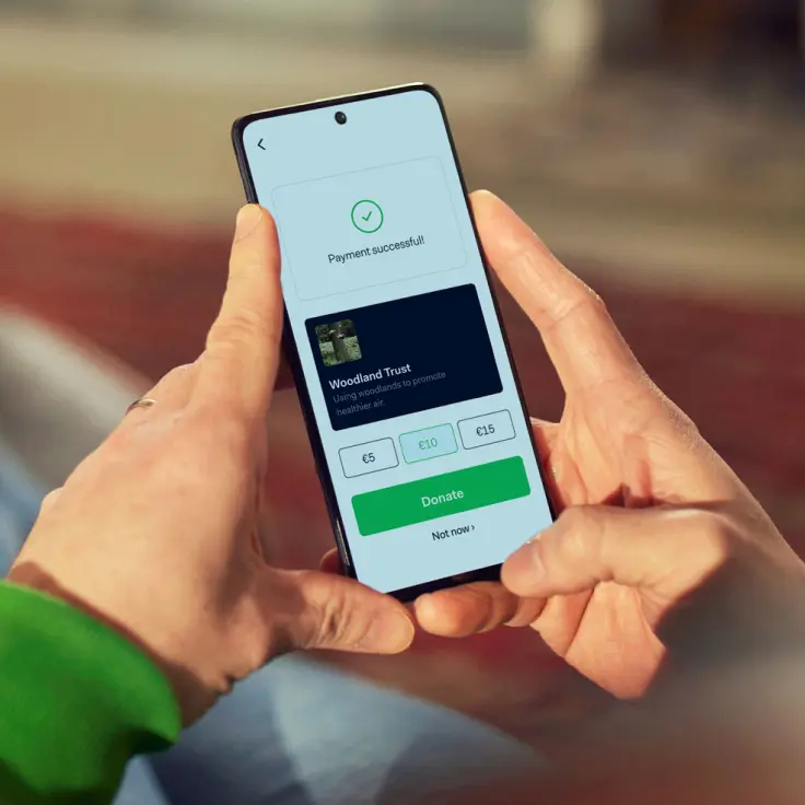 Person holding a smartphone displaying a successful payment notification for a donation to Woodland Trust.