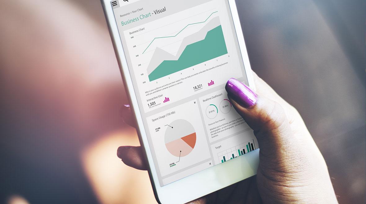 Primeiro plano de uma mão segurando um smartphone que exibe vários gráficos e tabelas de negócios.