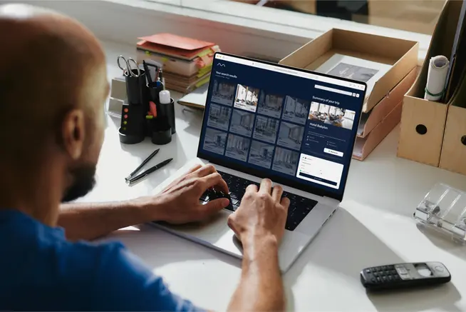 Um homem na frente de um laptop, a fazer uma reserva de hotel usando um sistema de reserva de agência de viagens online (OTA)