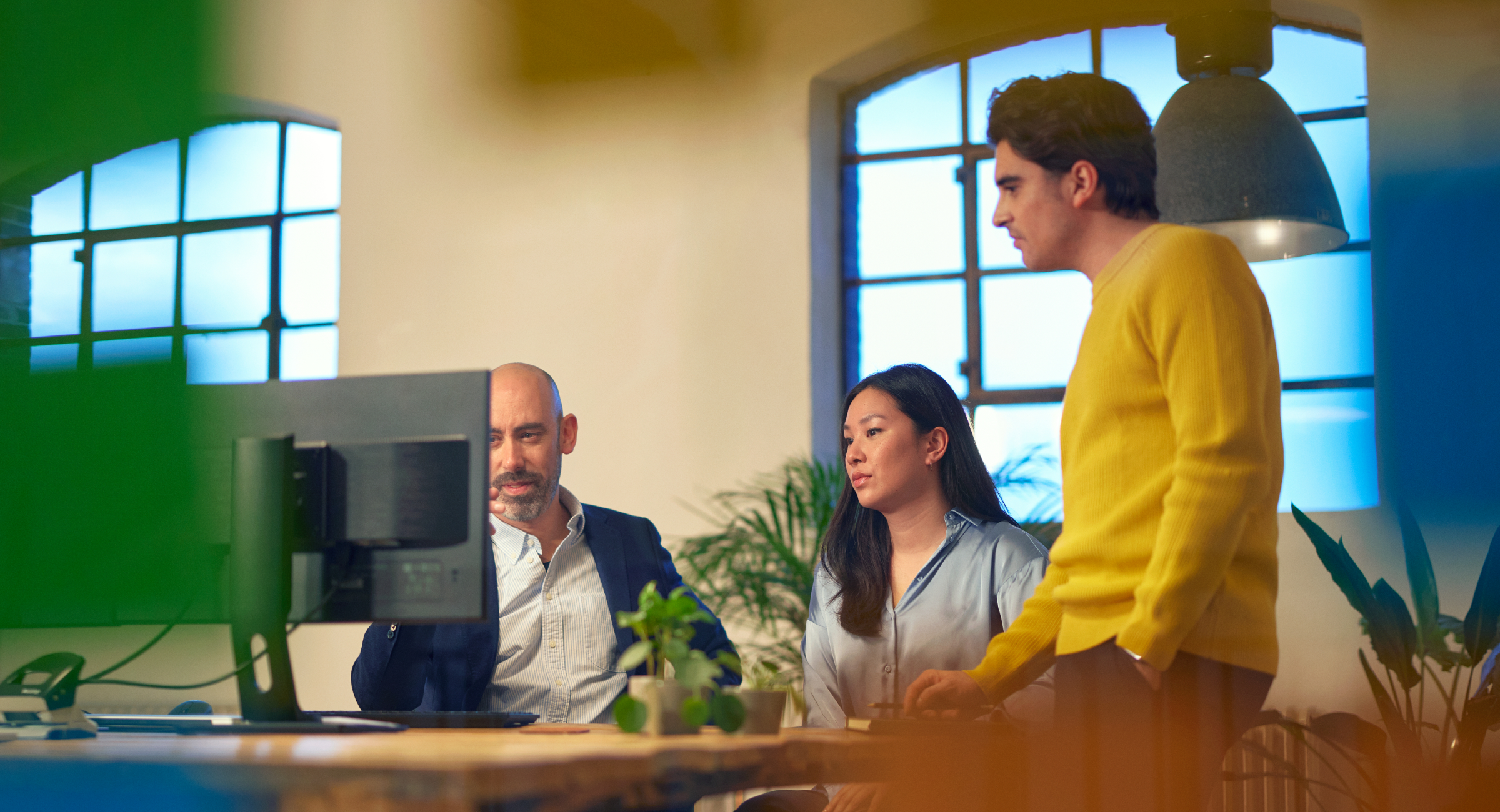 Three colleagues at a desk, staring at a monitor.
