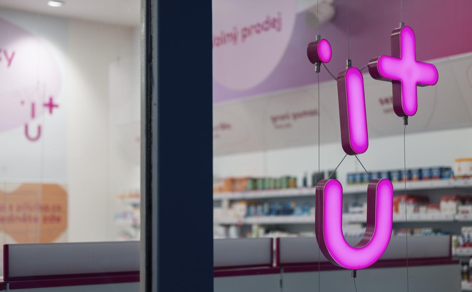 Růžově růžový kříž a plusový znak uvnitř lékárny viděný přes skleněné okno.
