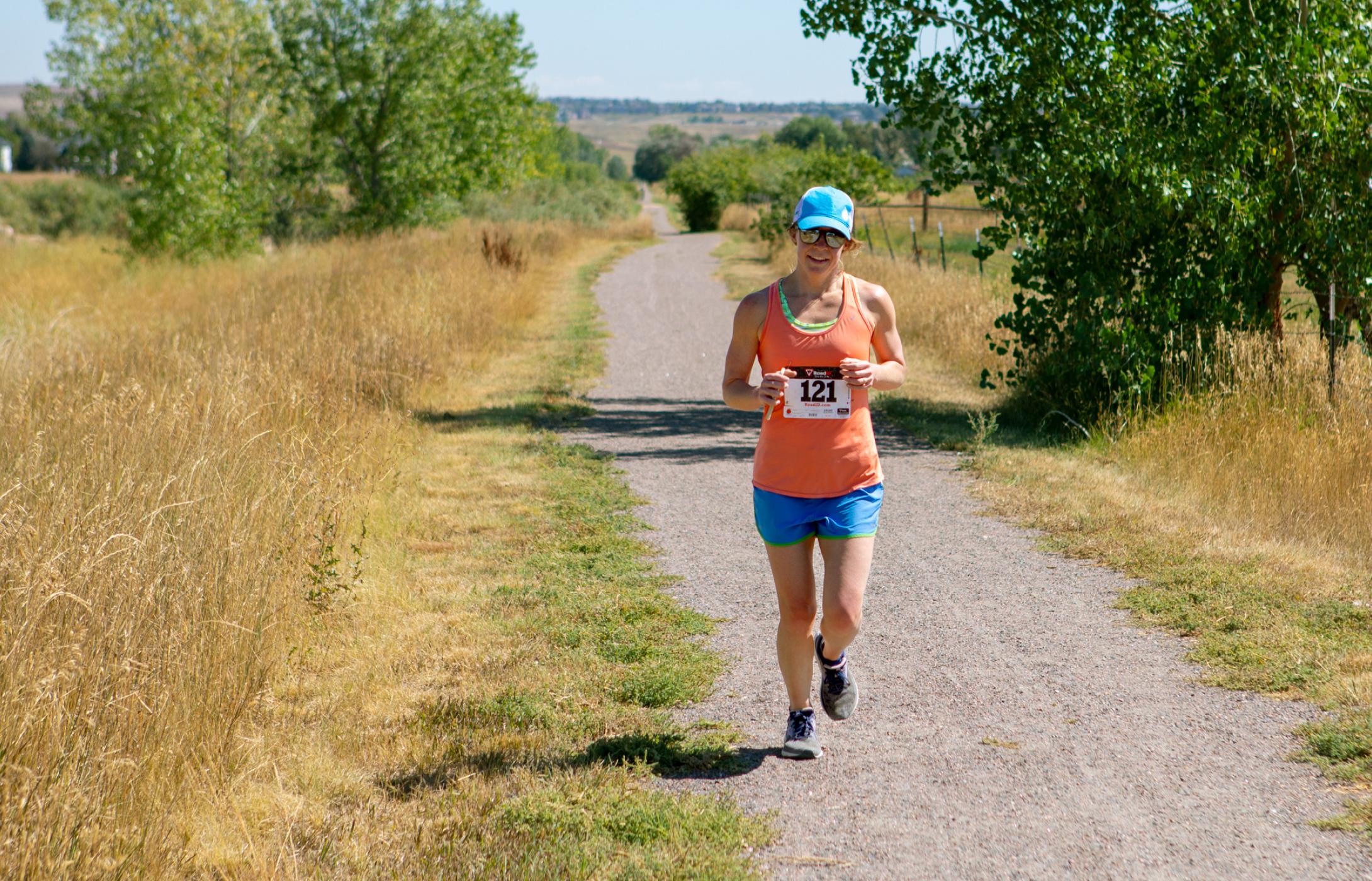 Female runner with bib number 121 jogging on a rural trail.