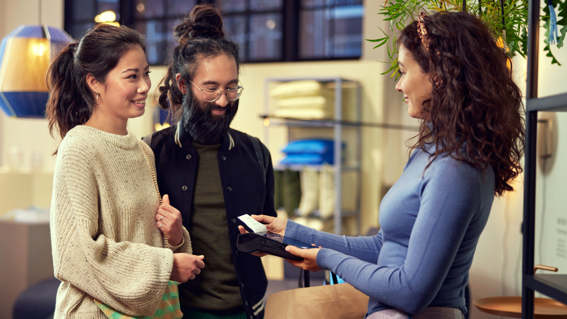Um casal sorridente fazendo um pagamento com uma caixa feminina usando um leitor de cartão portátil.