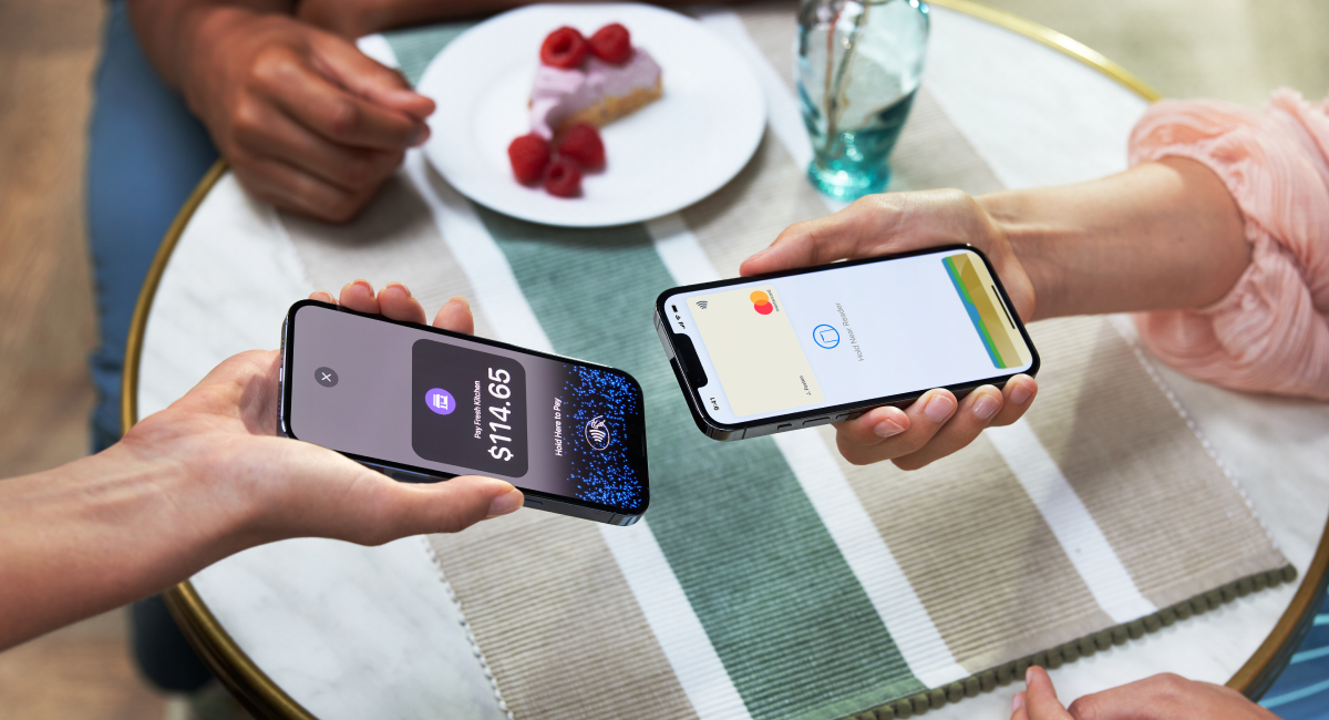 Two individuals making a contactless payment using a smartphone and a portable card reader.