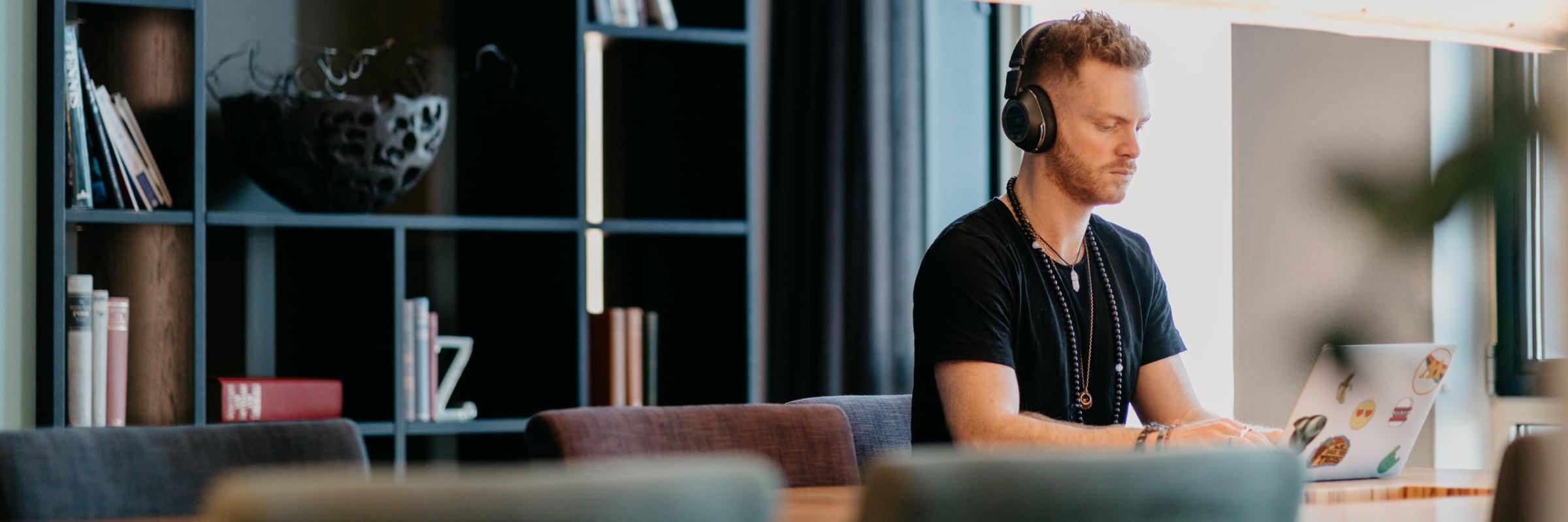 Man using laptop with headphones in a modern office setting.