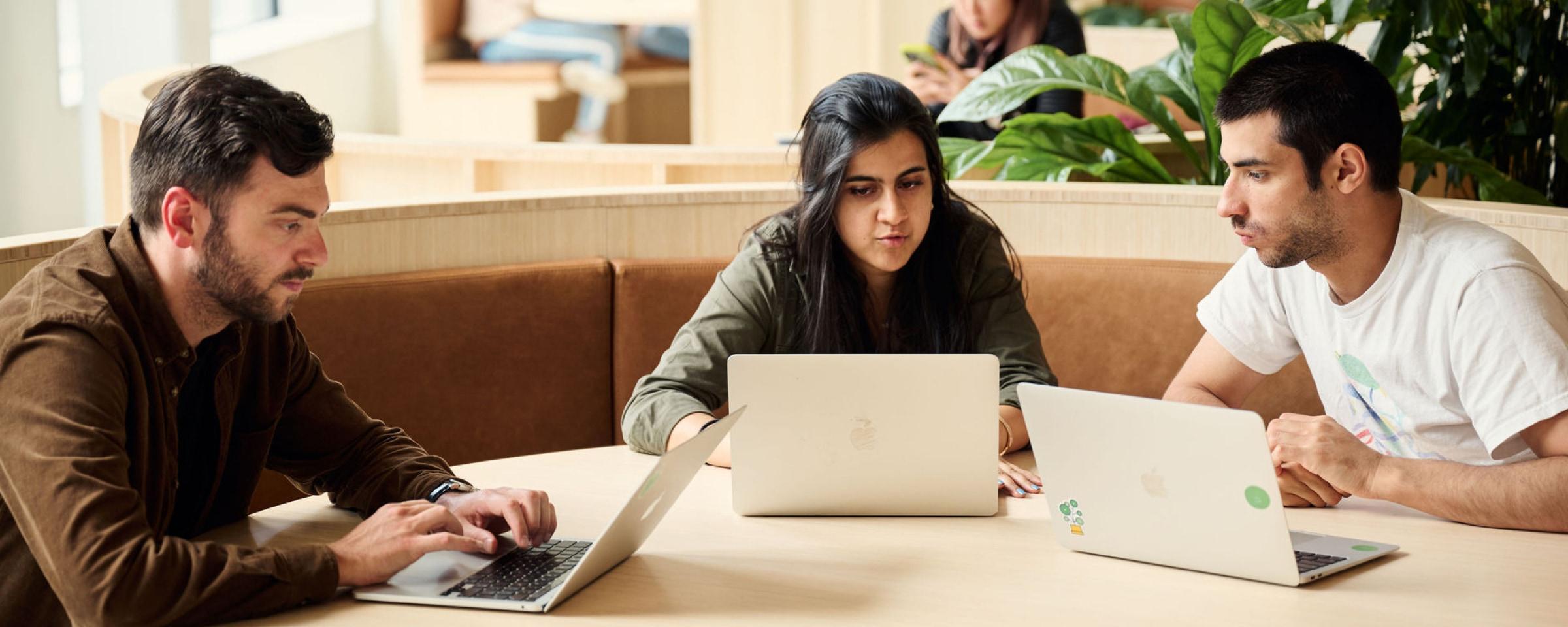Tre kolleger som samarbeider over bærbare datamaskiner på et trebord.