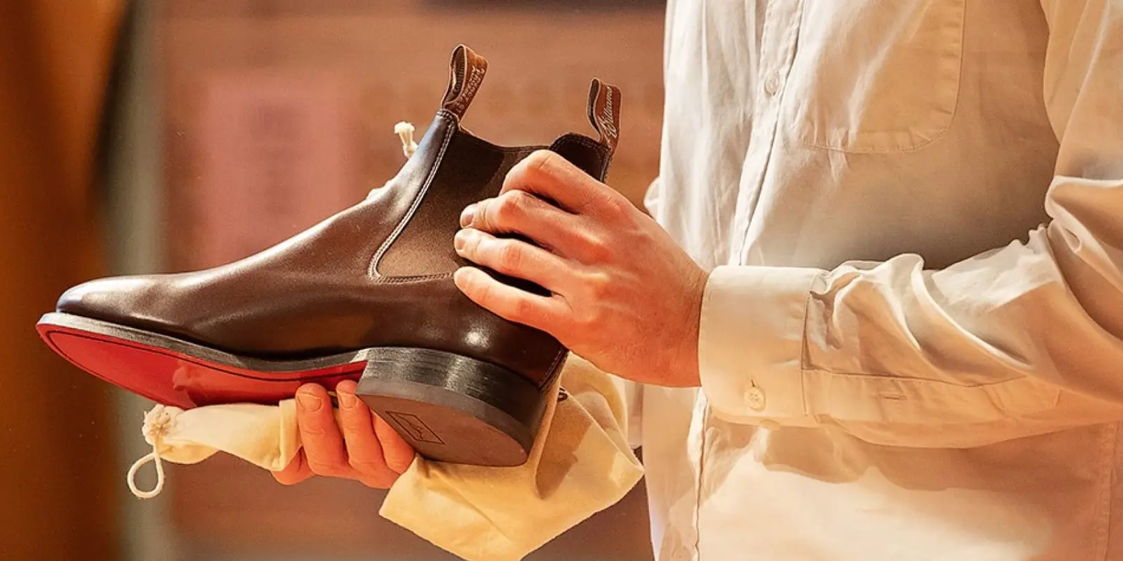 Person holding a polished brown leather boot with red trim over a buffing cloth.