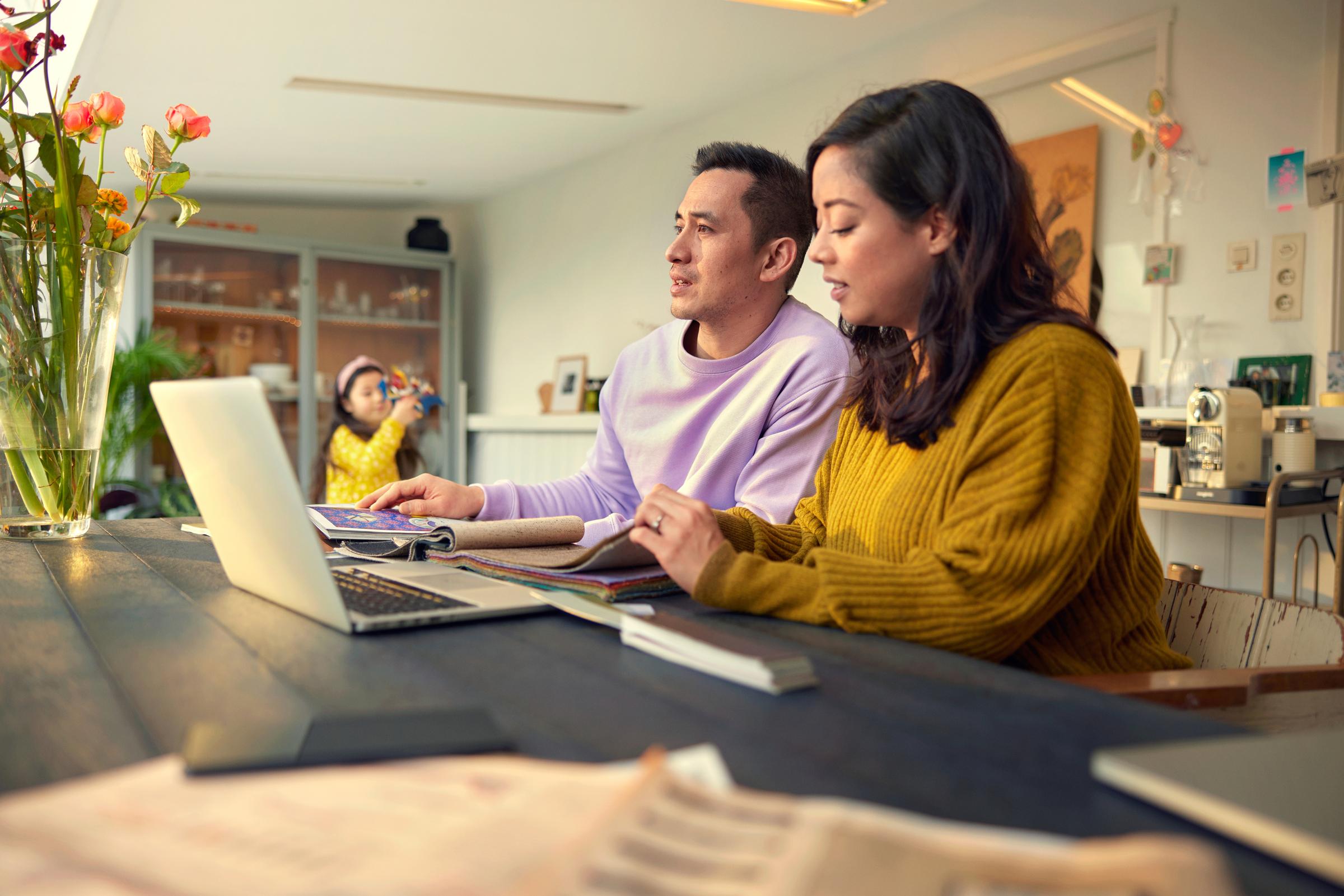 Couple with kids sitting at a table in front of a laptop choosing a fabric for their home furnishing.