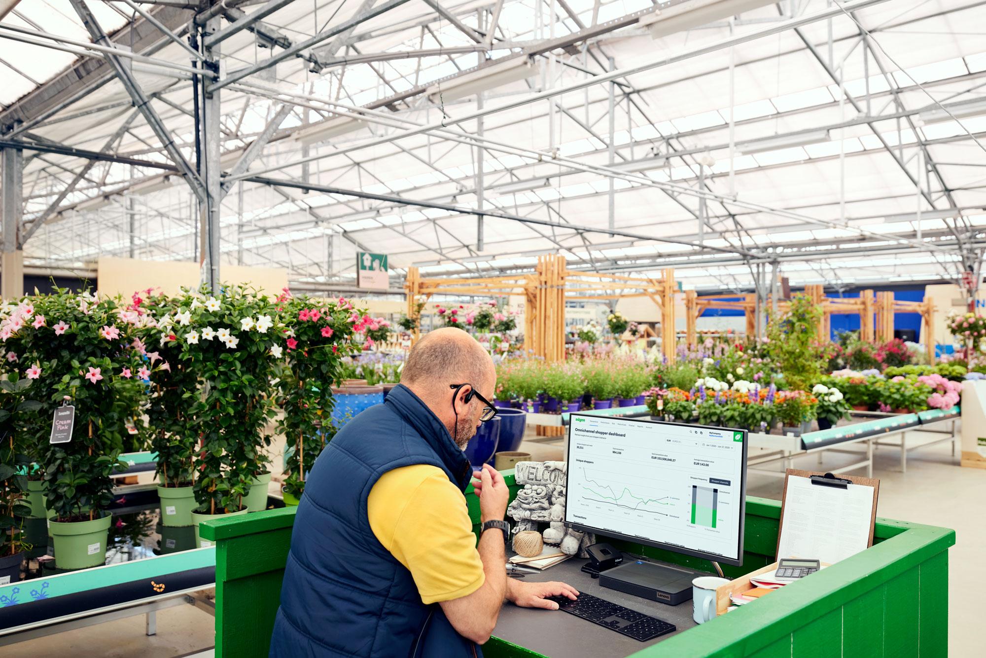 Um funcionário num centro de jardinagem a olhar para um painel Adyen num computador.