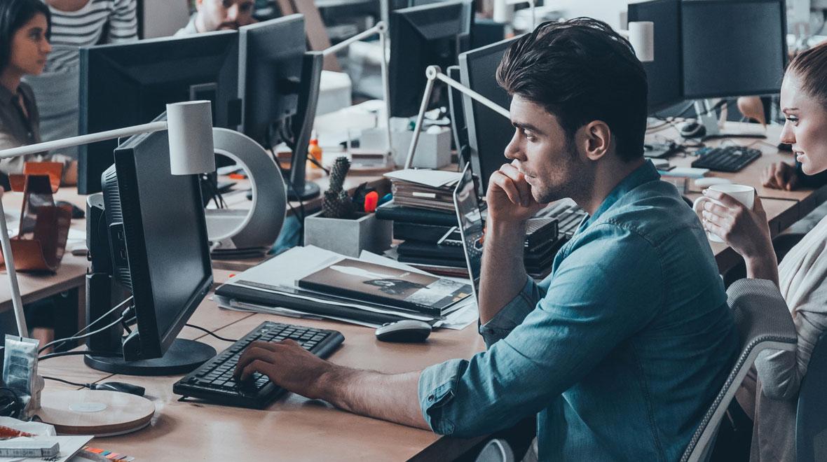 Homem e mulher trabalhando em computadores em um ambiente de escritório movimentado