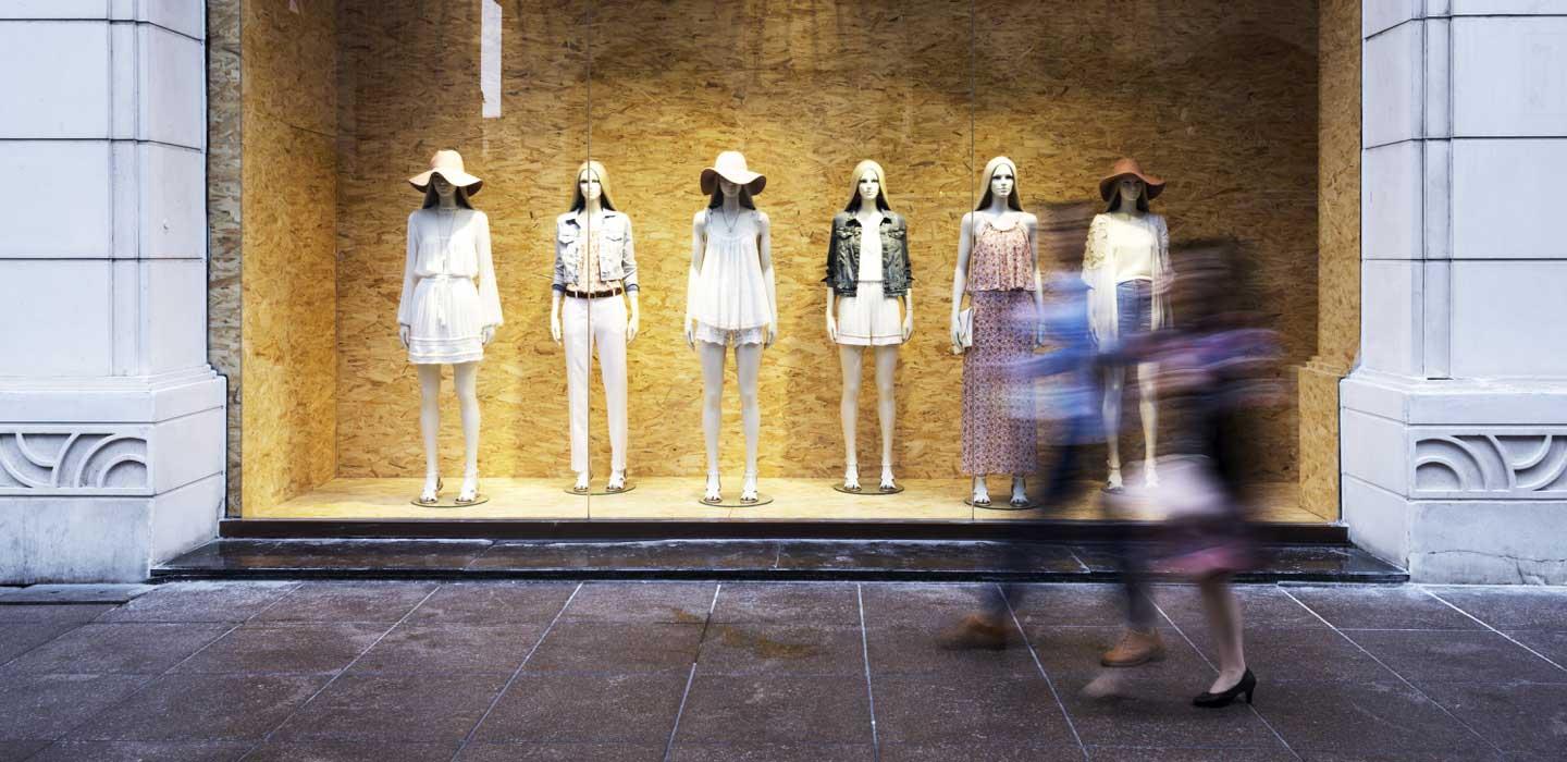 Figure sfocate che camminano davanti a un negozio con manichini che mostrano abbigliamento alla moda
