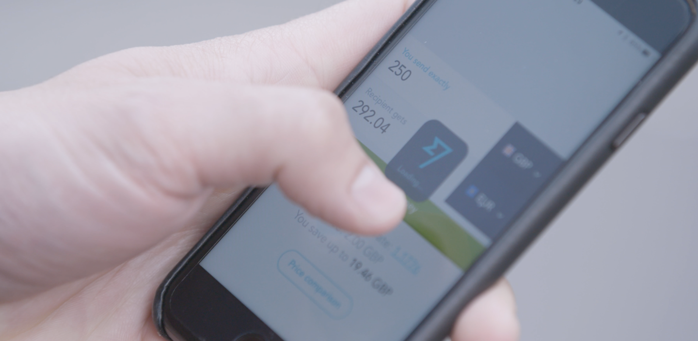 Närbild av en hand som håller i en smartphone med valutakurser