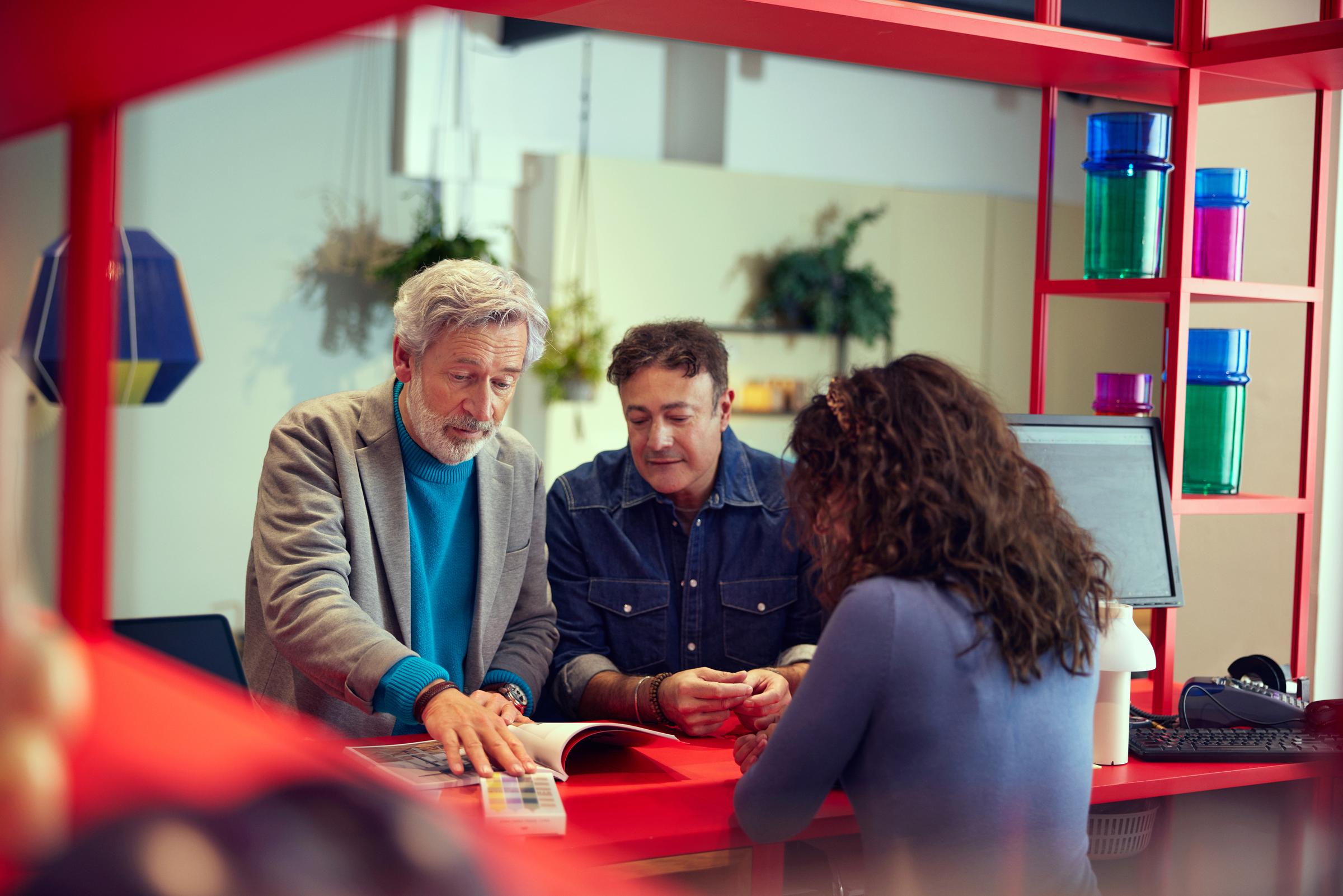 To menn diskuterer farge mønstre med en salgsassistent over disken i en hjemmevare og møbelbutikk.