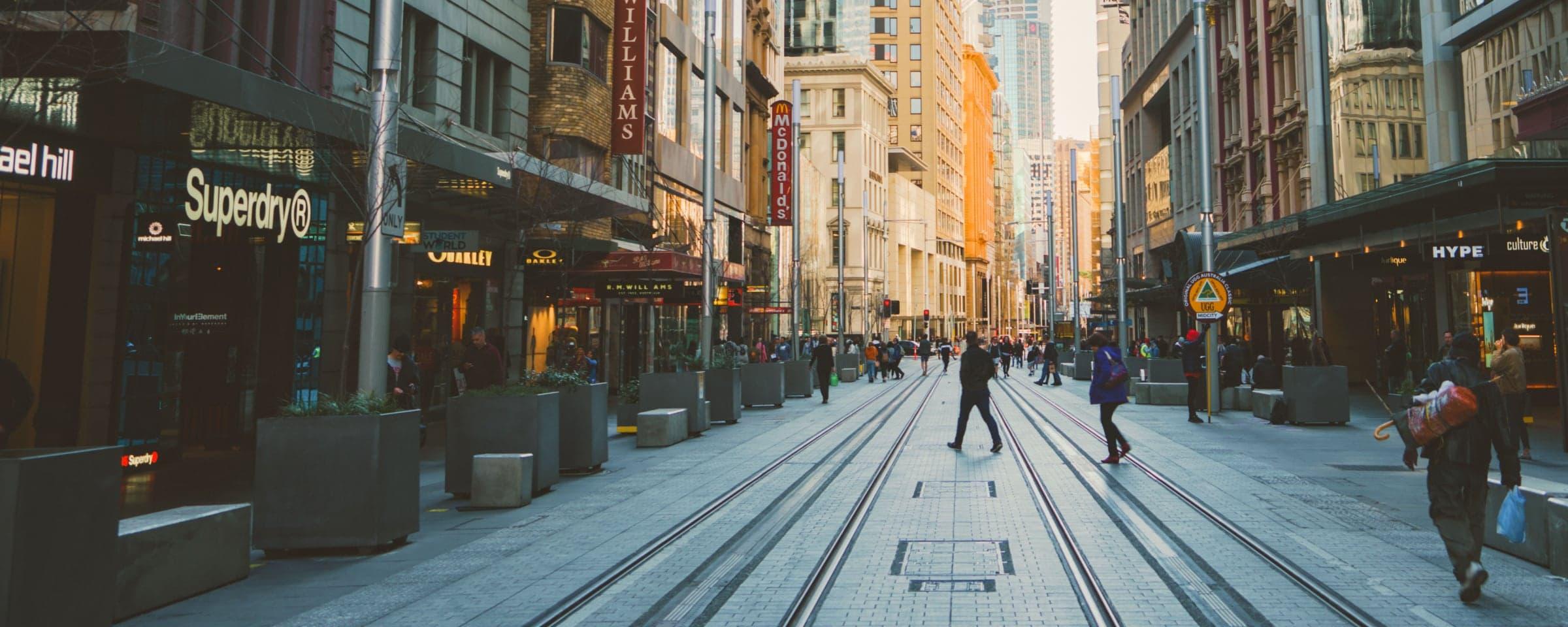 Beskæftiget bygade med sporvognsspor og mennesker, der går forbi butikker om dagen