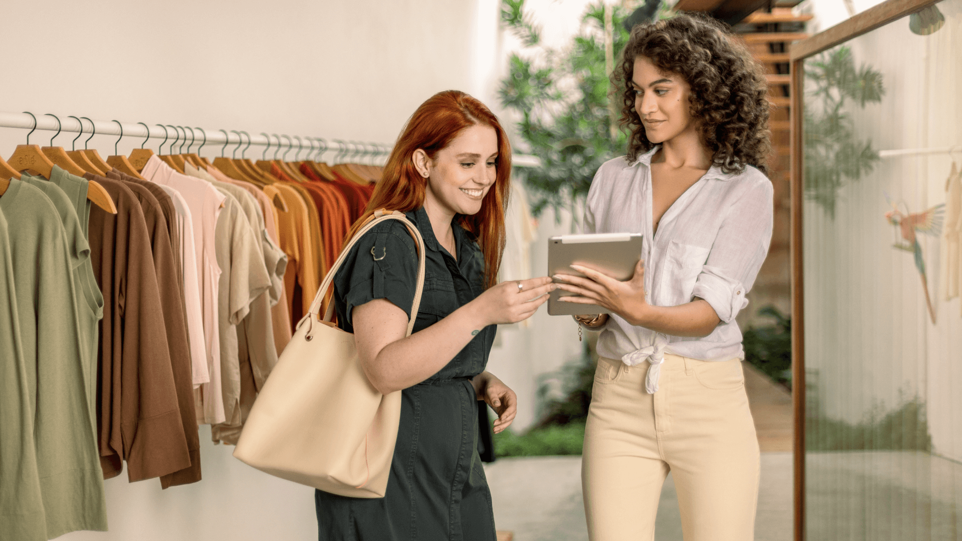 Duas mulheres em uma loja de roupas, uma segurando um tablet com o sistema de pagamento da Adyen.