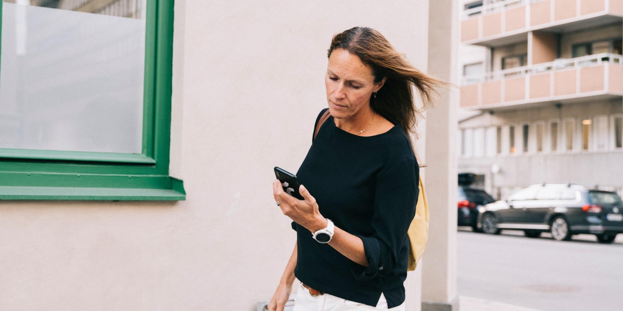 Woman walking and looking at her phone on a city street.