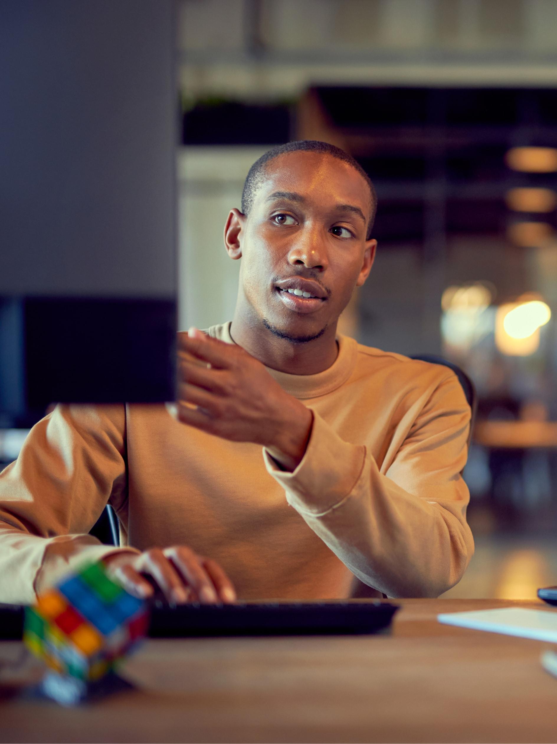 Man gesturing during a conversation while working on a laptop with a Rubik's cube on the desk