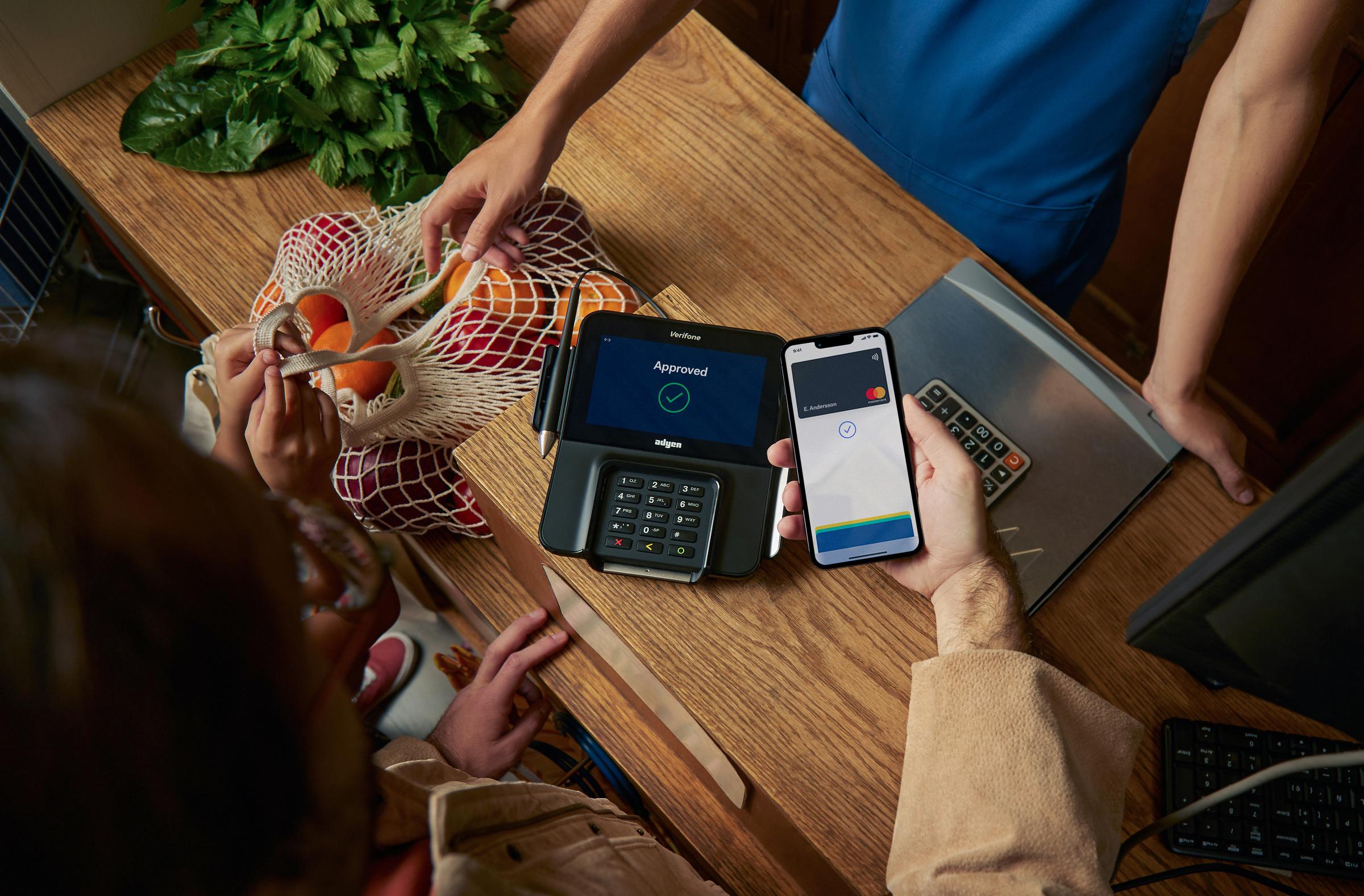 Person making a contactless payment using a mobile phone to a card terminal displaying 'Approved' by Adyen.