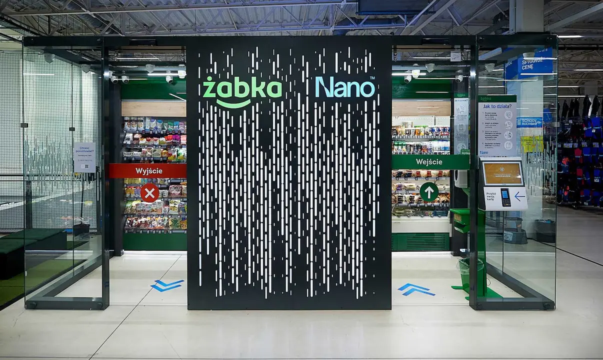 Wejście do sklepu Zabka Nano z automatycznymi drzwiami szklanymi i plakatami informacyjnymi.