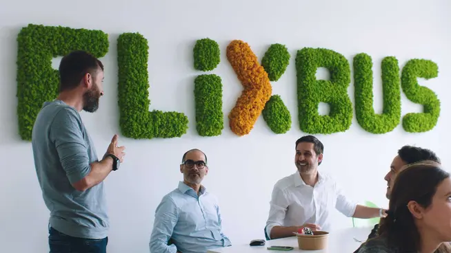 Team meeting with a man presenting and the FlixBus logo on the wall made of greenery.