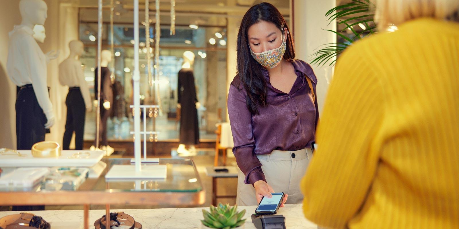 Customer wearing a mask making a contactless payment at a store.
