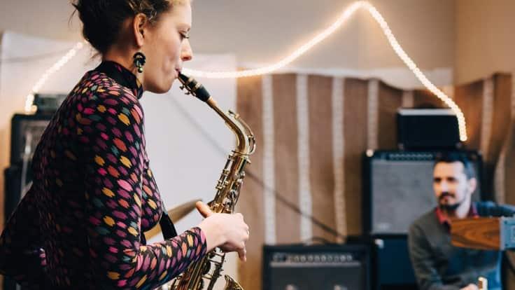 Kobieta grająca na saksofonie w zespole z męskim gitarzystą w tle
