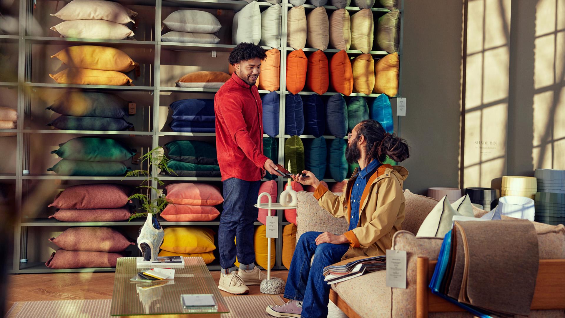 Two people in a cozy home decor store with colorful cushions and a payment transaction taking place.