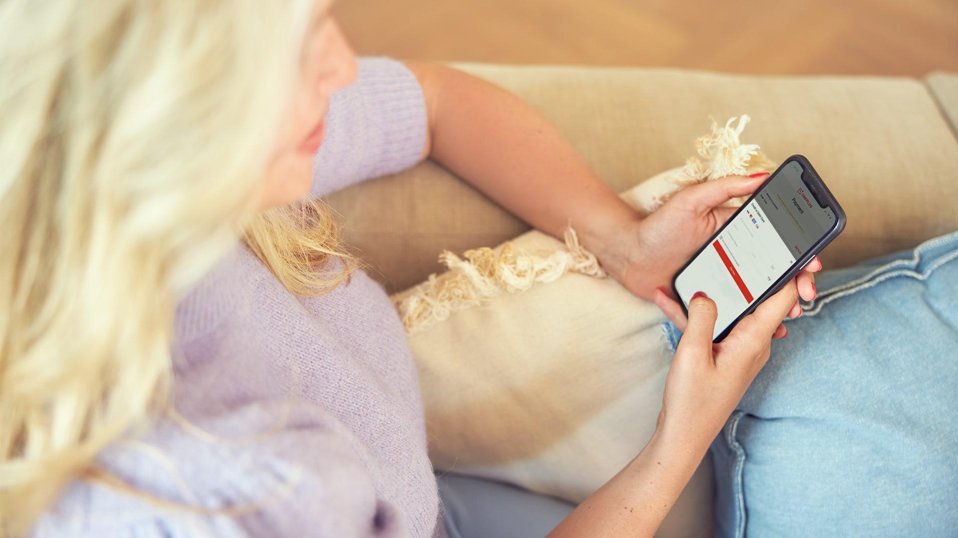 Person sitting on a couch using smartphone with Adyen checkout screen.