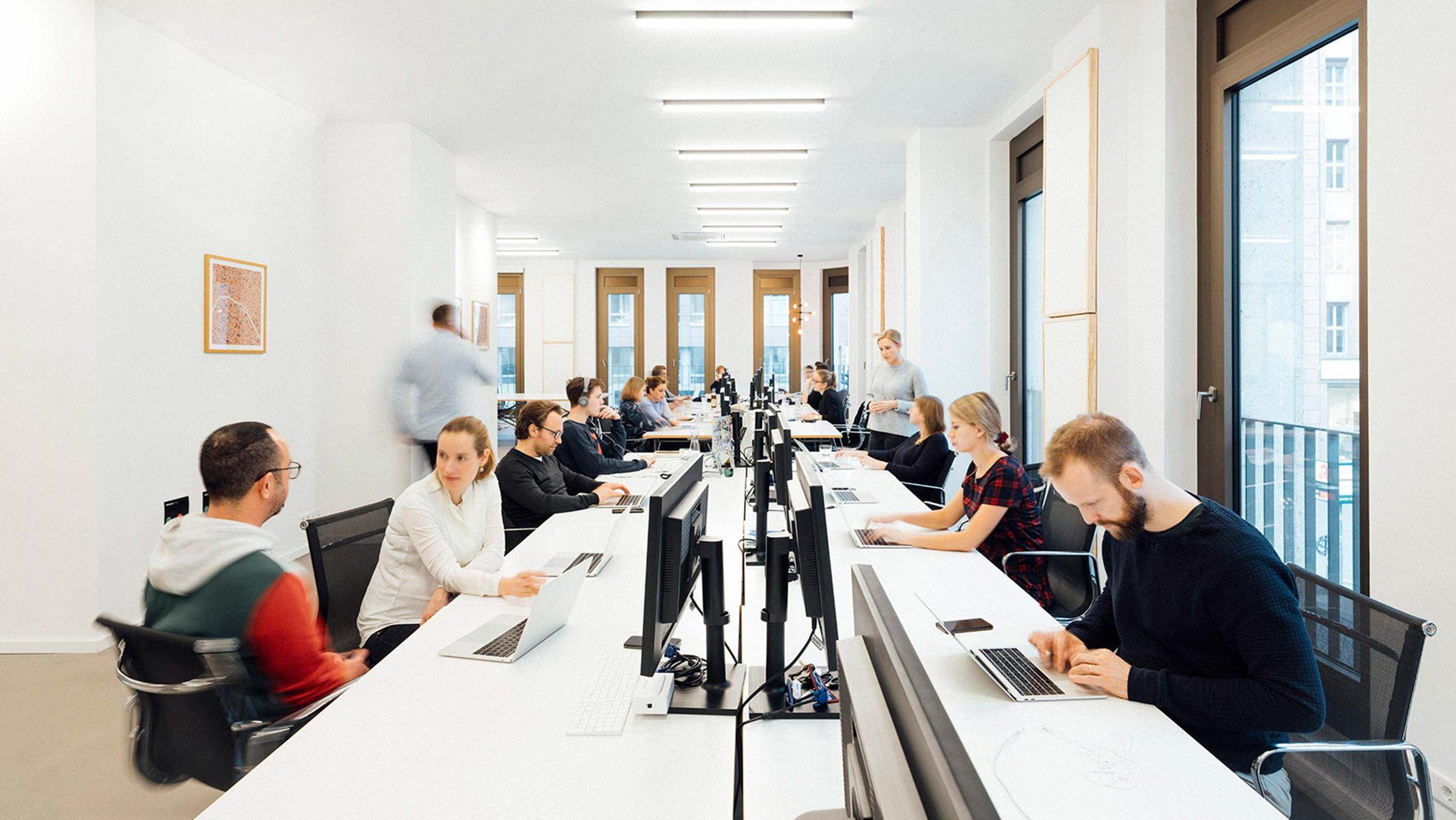 Menschen arbeiten an einem langen Bürotisch mit Laptops.