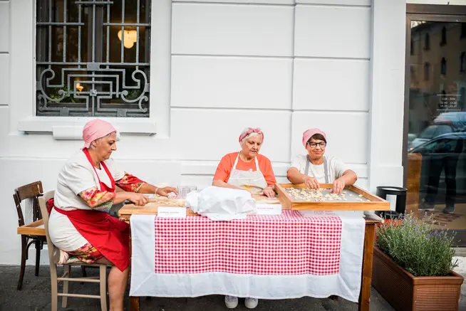 Tre donne sedute a un tavolo fuori da una casa che preparano cibo