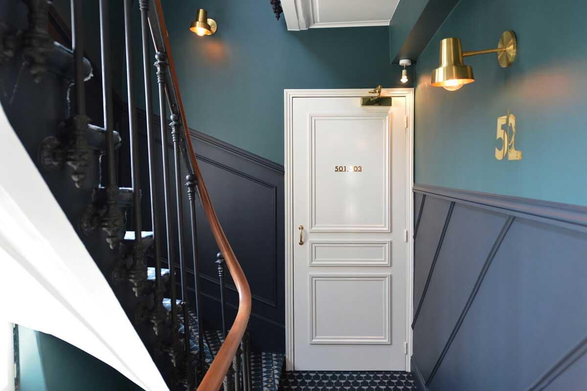 Intérieur élégant avec une porte blanche marquée '501.03', un escalier et des lampes murales dorées.