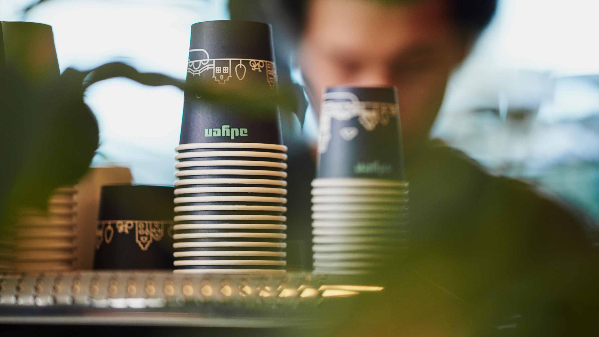 Stacked paper cups with blurred foreground and person in background.