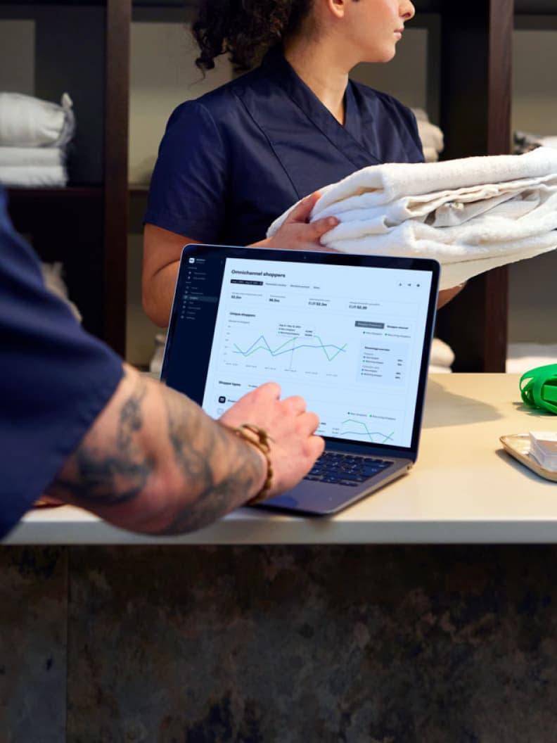 Person holding folded towels with a laptop displaying Adyen analytics graphs on the screen.