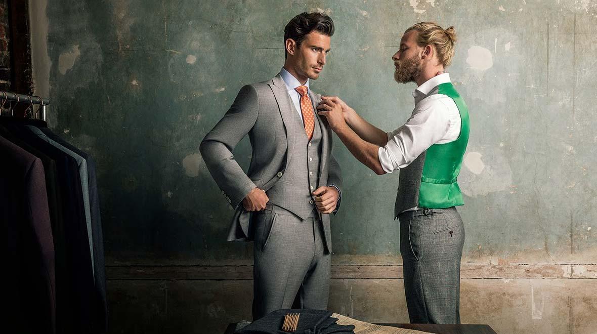 Tailor fitting a stylish grey suit on a gentleman in a workshop.