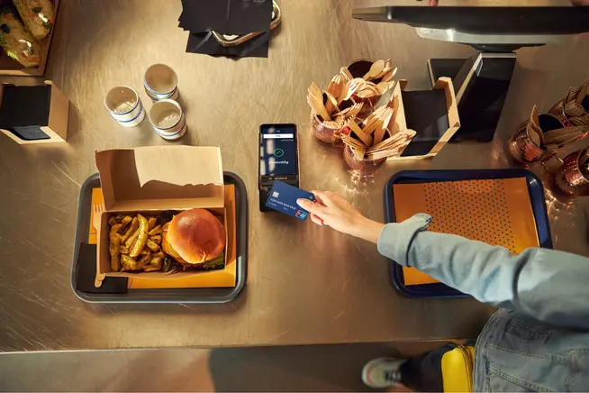 Osoba používající smartphone k provedení bezkontaktní platby s terminálem Adyen v restauraci