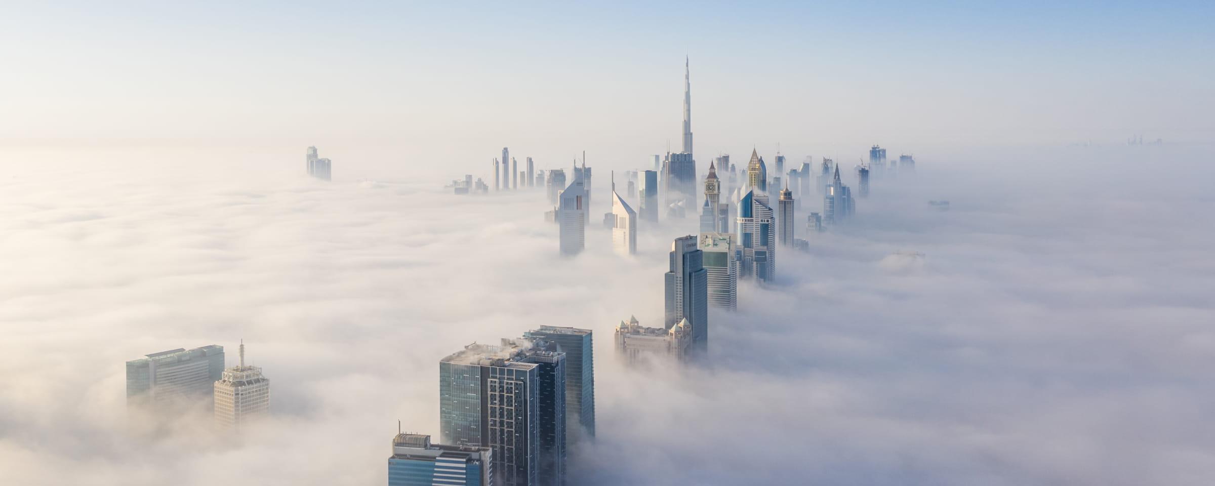 Skyscrapers piercing through a thick blanket of clouds at sunrise.