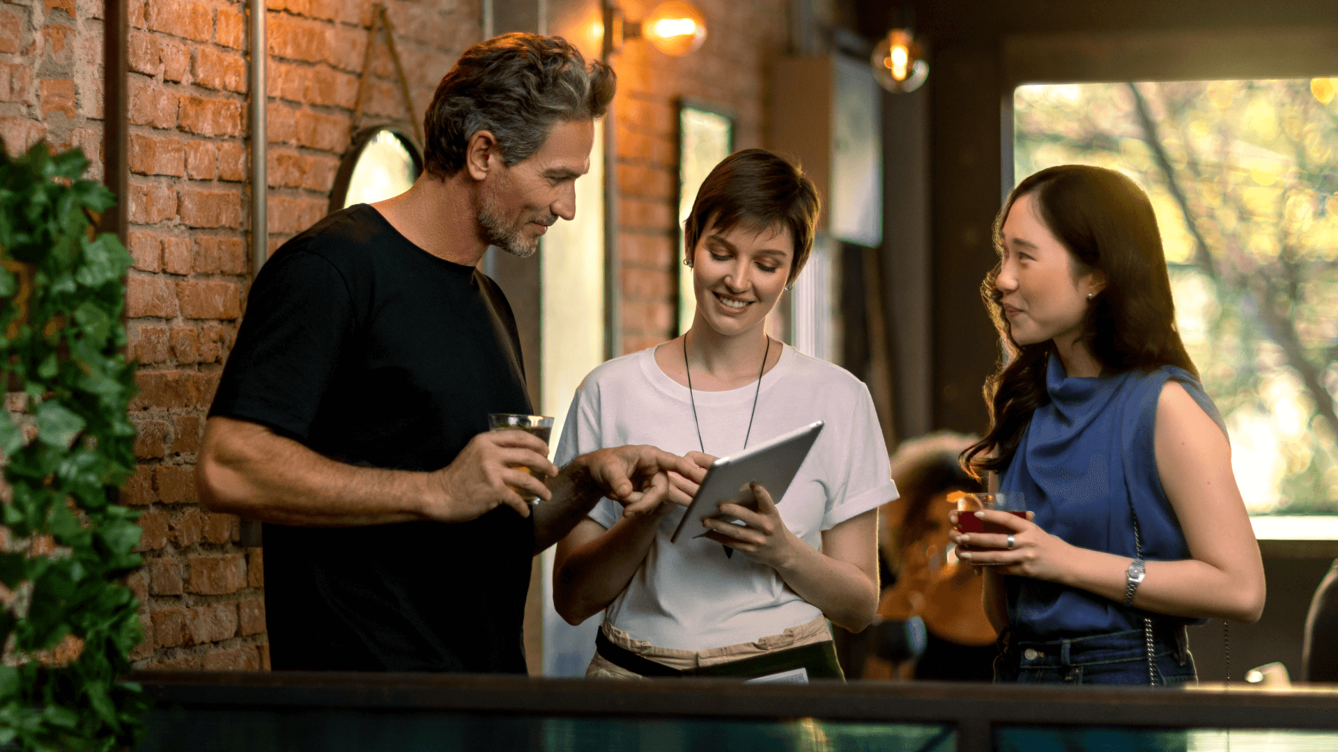 Duas mulheres e um homem interagindo com um tablet digital em um café