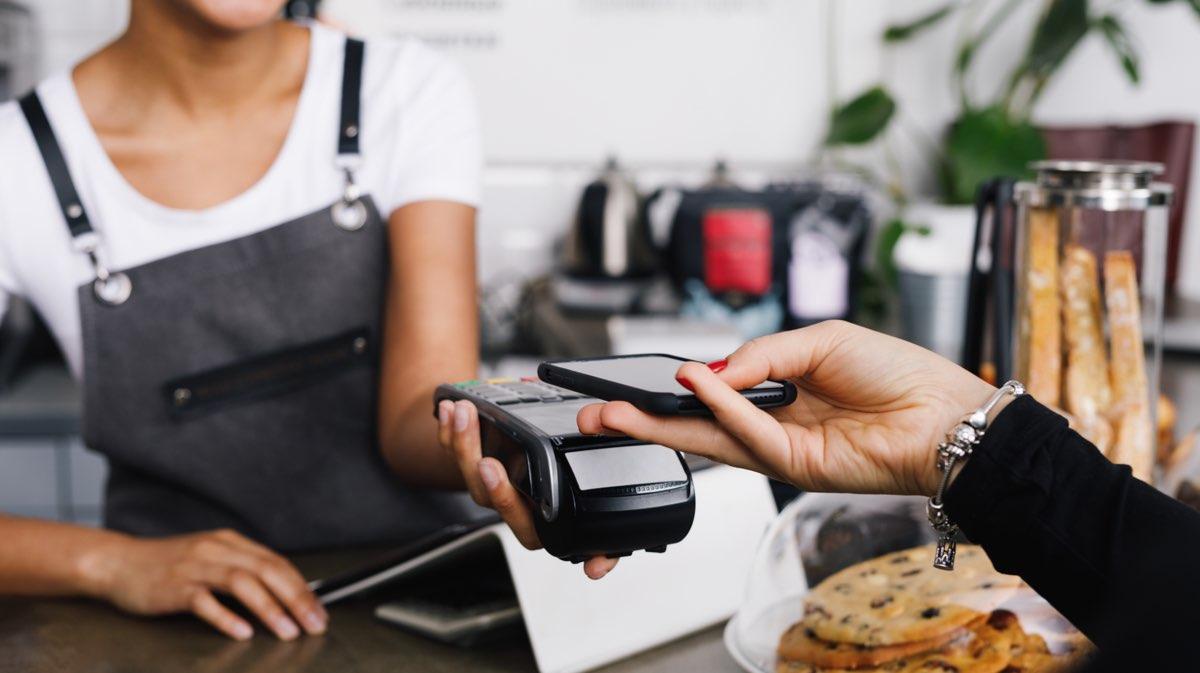 Kund som gör ett kontaktlöst betalning med en telefon över en kassaapparat