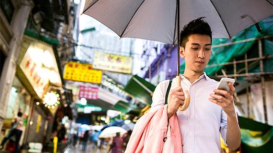 Jeune homme avec un parapluie regardant son smartphone dans une rue animée de la ville la nuit.