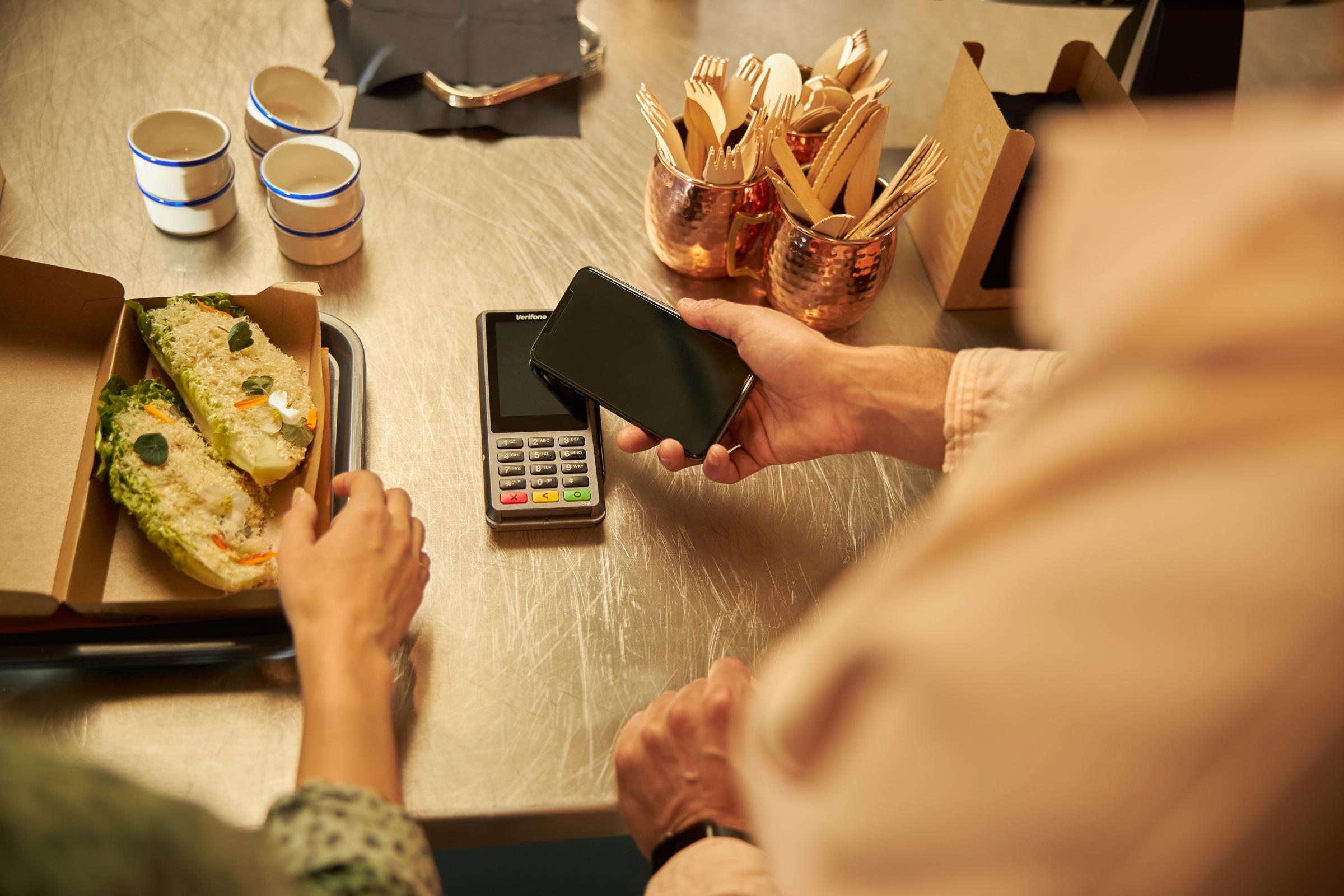 Person som gör en kontaktlös betalning med en telefon vid en kassa