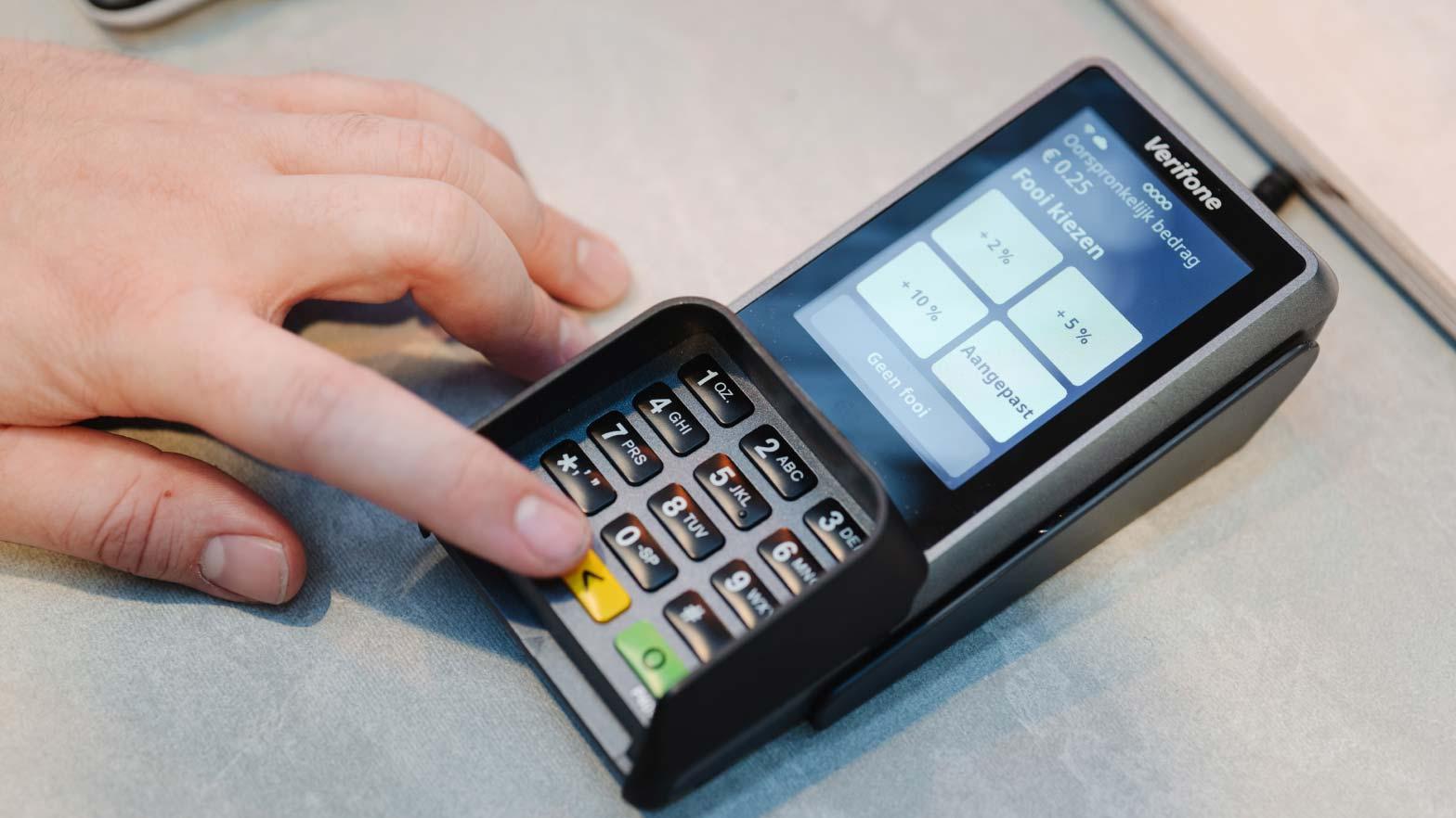 Close-up of a hand using an Adyen card terminal with tip options on the screen.