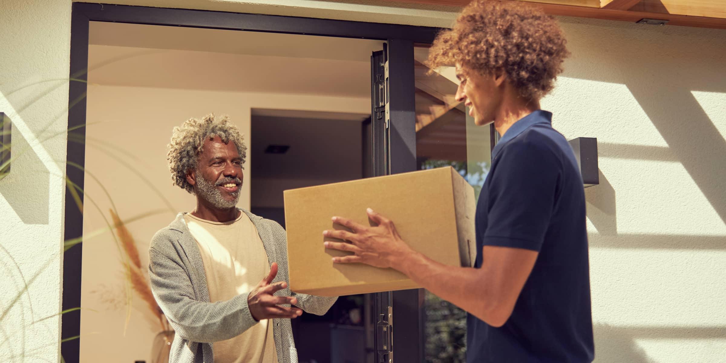 Smiling older man receiving a package from a delivery person at his doorstep.