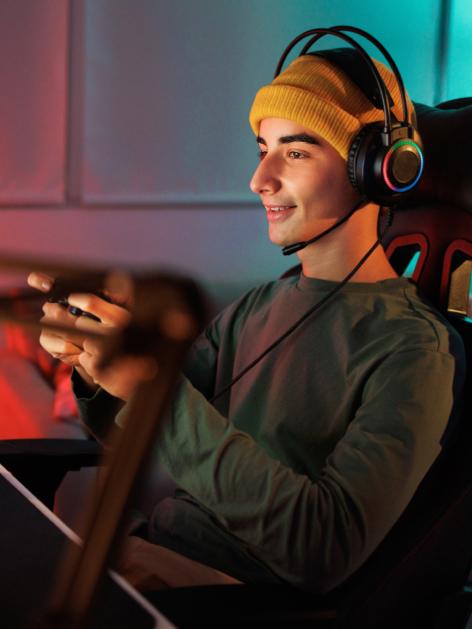 Smiling person in gaming chair wearing headset and holding a gaming controller.